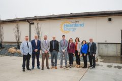 Group of people stand in front of building with Heartland Energy logo