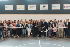 Crowd stands with ceremonial ribbon as it is being cut