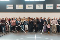 Crowd stands with ceremonial ribbon as it is being cut