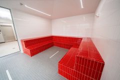 Interior of large white steam room with red seating along three walls.