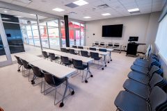 Interior meeting room with three long tables, seating and a tv on the wall.