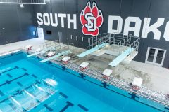 Diving boards and starting blocks for a large indoor pool with the USD logo on the wall behind.